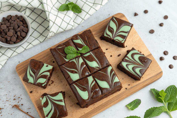 The Ultimate Chocolate Mint Brownies 1 Rich and fudgy chocolate mint brownies topped with a smooth chocolate ganache and garnished with fresh mint leaves, served on a white plate