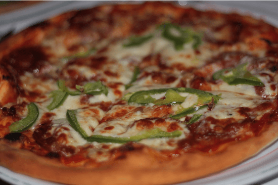 A beautifully baked pizza all-dressed served on a wooden board, garnished with fresh basil